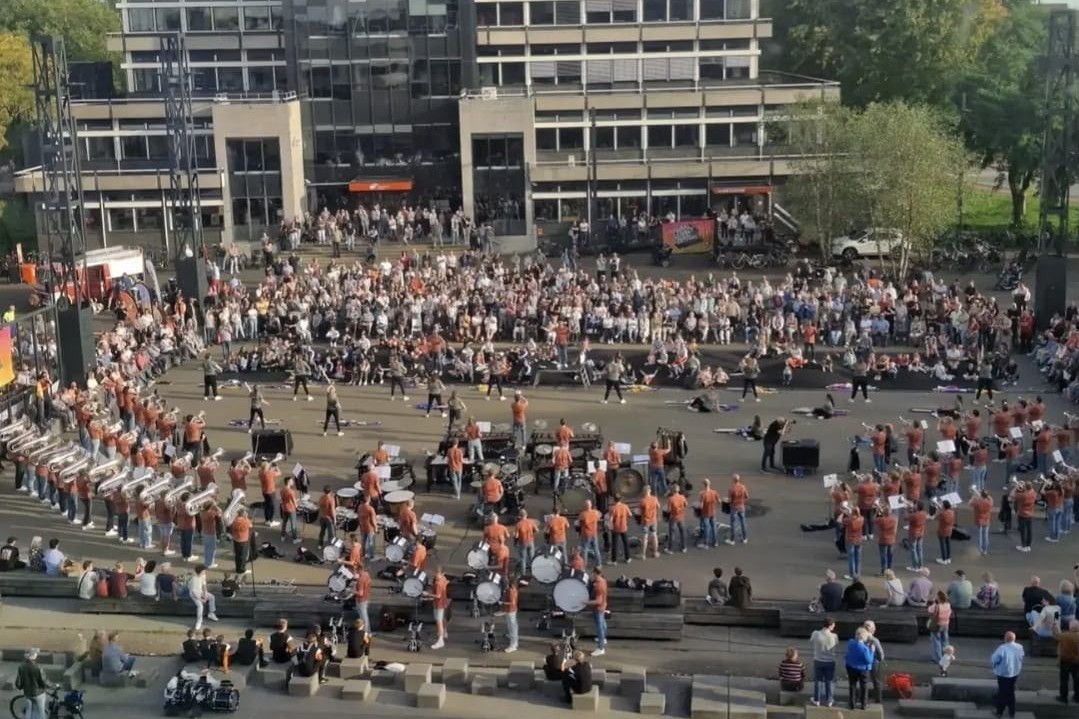 Het Jubal Legacy Project tijdens een optreden in 2026, van bovenaf gezien: hornline, slagwerk en color guard in oranje shirts voor een groot publiek